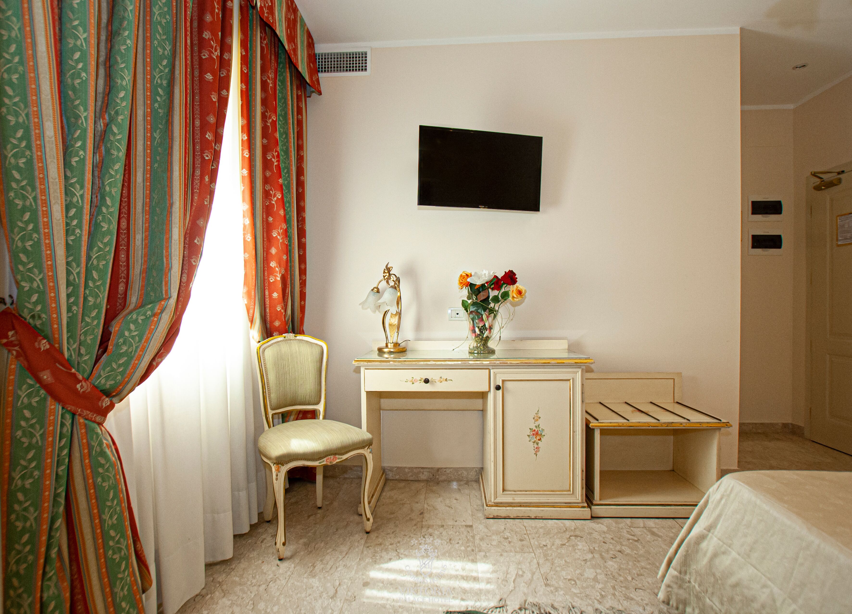 Une chambre d’hôtel équipée d’un bureau, d’une chaise, d’un lit et d’un téléviseur à écran plat fixé au mur.