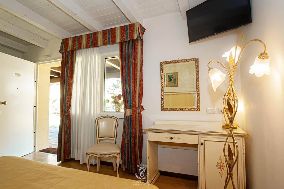 Hotellihuone, jossa on sänky, työpöytä, tuoli, televisio ja koristeellinen lamppu.