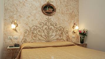 Ein Hotelzimmer mit einem Bett, einem Nachttisch mit Lampe, einem an der Wand befestigten Spiegel und einer Blumenvase.