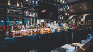 Zona de bar con estantes llenos de botellas de licores, vasos y utensilios.