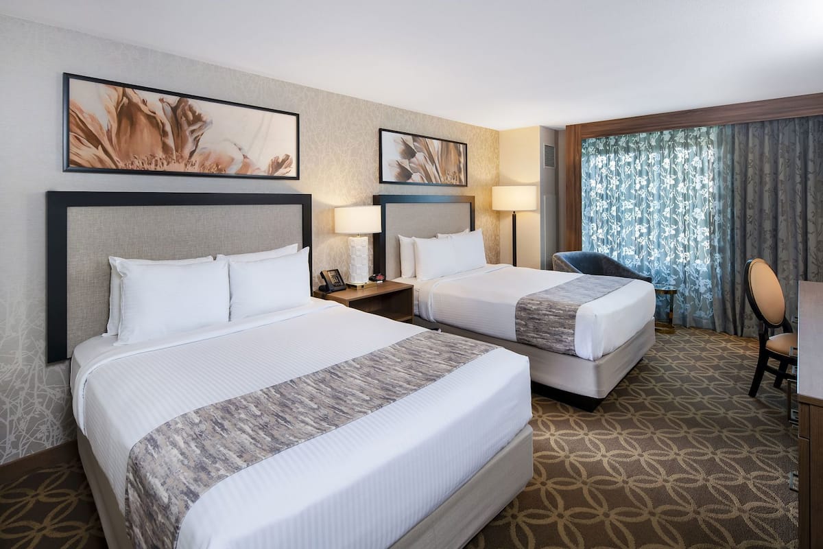 A hotel room with two beds, a desk, a chair, and artwork on the walls.