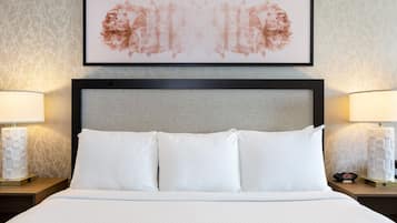 Un lit bien fait, avec du linge de lit blanc, deux tables de chevet avec des lampes et une œuvre d’art encadrée au-dessus du lit.