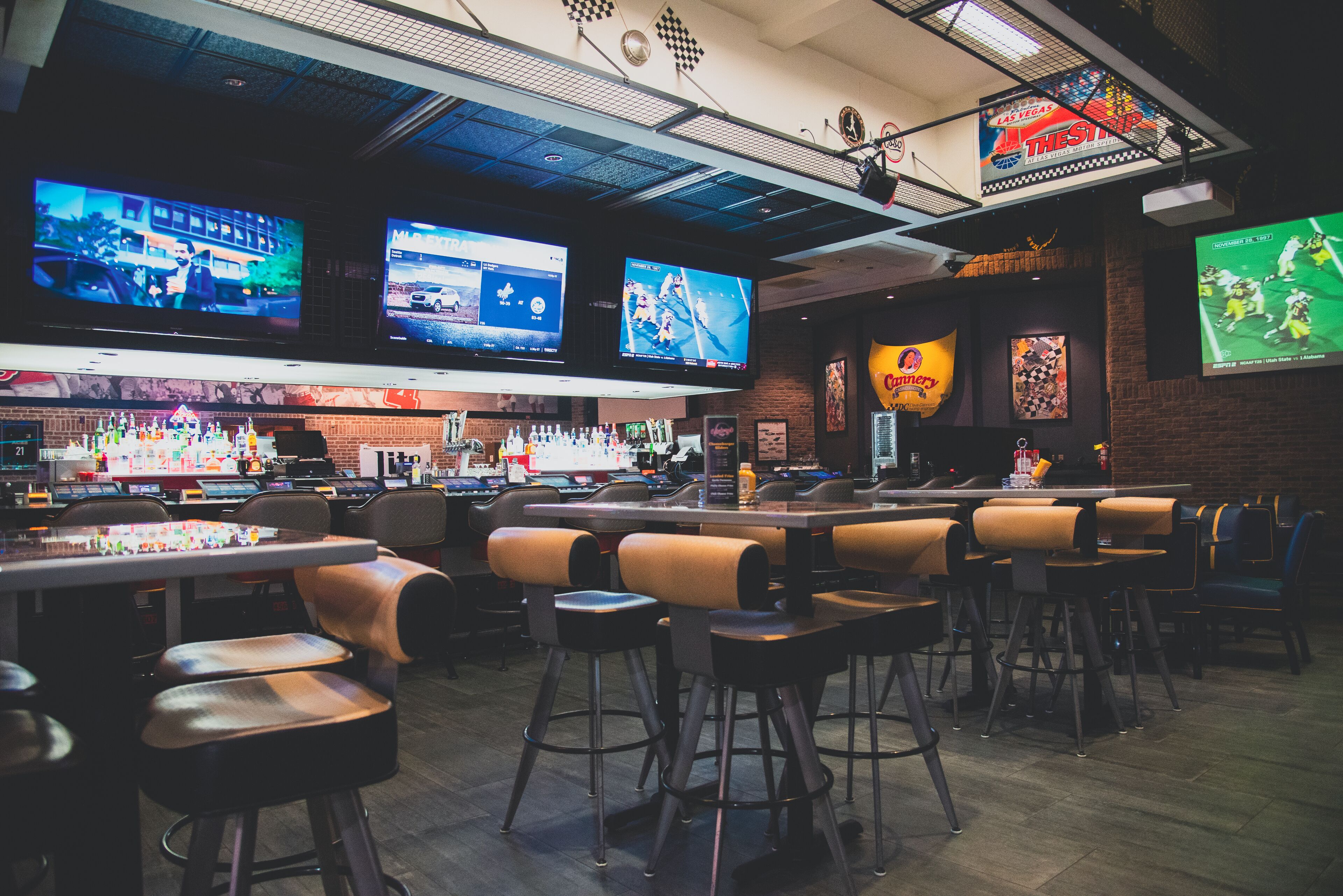 A bar area with multiple screens displaying sports, a counter with a variety of beverages, and several seating options.