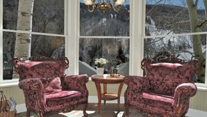 A bay window with two ornate chairs and a small table, overlooking a snowy landscape. - The Victorian Inn (Telluride)