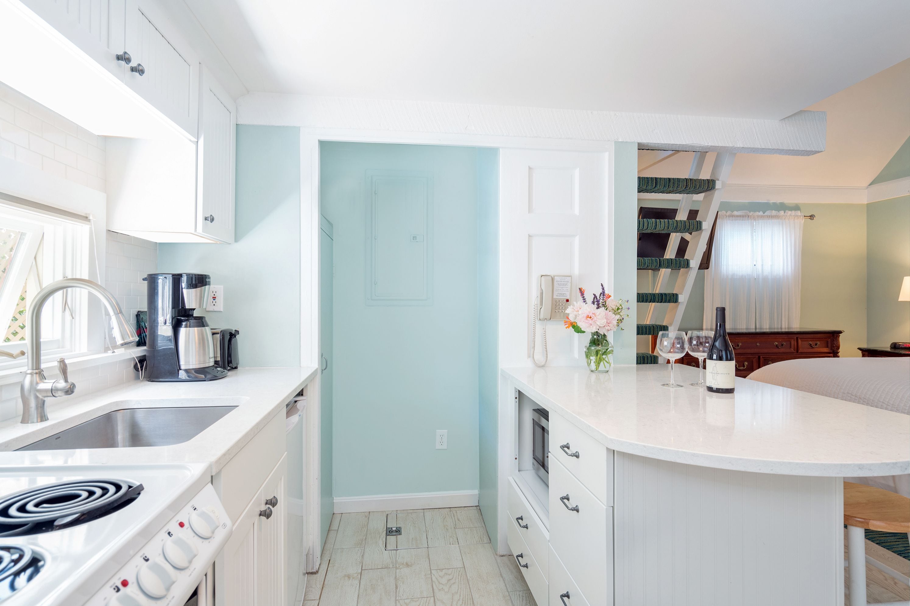 A compact kitchen with white cabinets, a stove, and a sink. There is a small island with a vase of flowers and a bottle of wine.