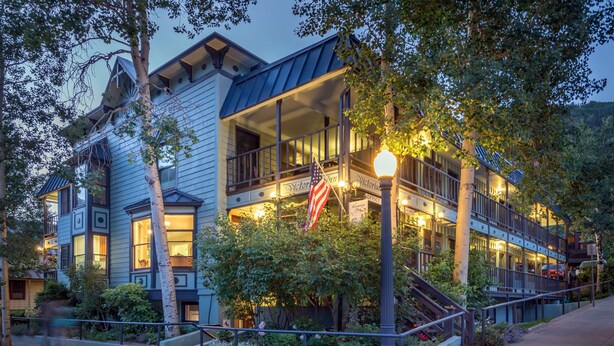 A multi-story building with a porch, a flag, and a street lamp. - The Victorian Inn (Telluride)
