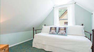 A bedroom with a sloped ceiling, a bed with white bedding, two decorative pillows, a wooden nightstand, and a window with white curtains.