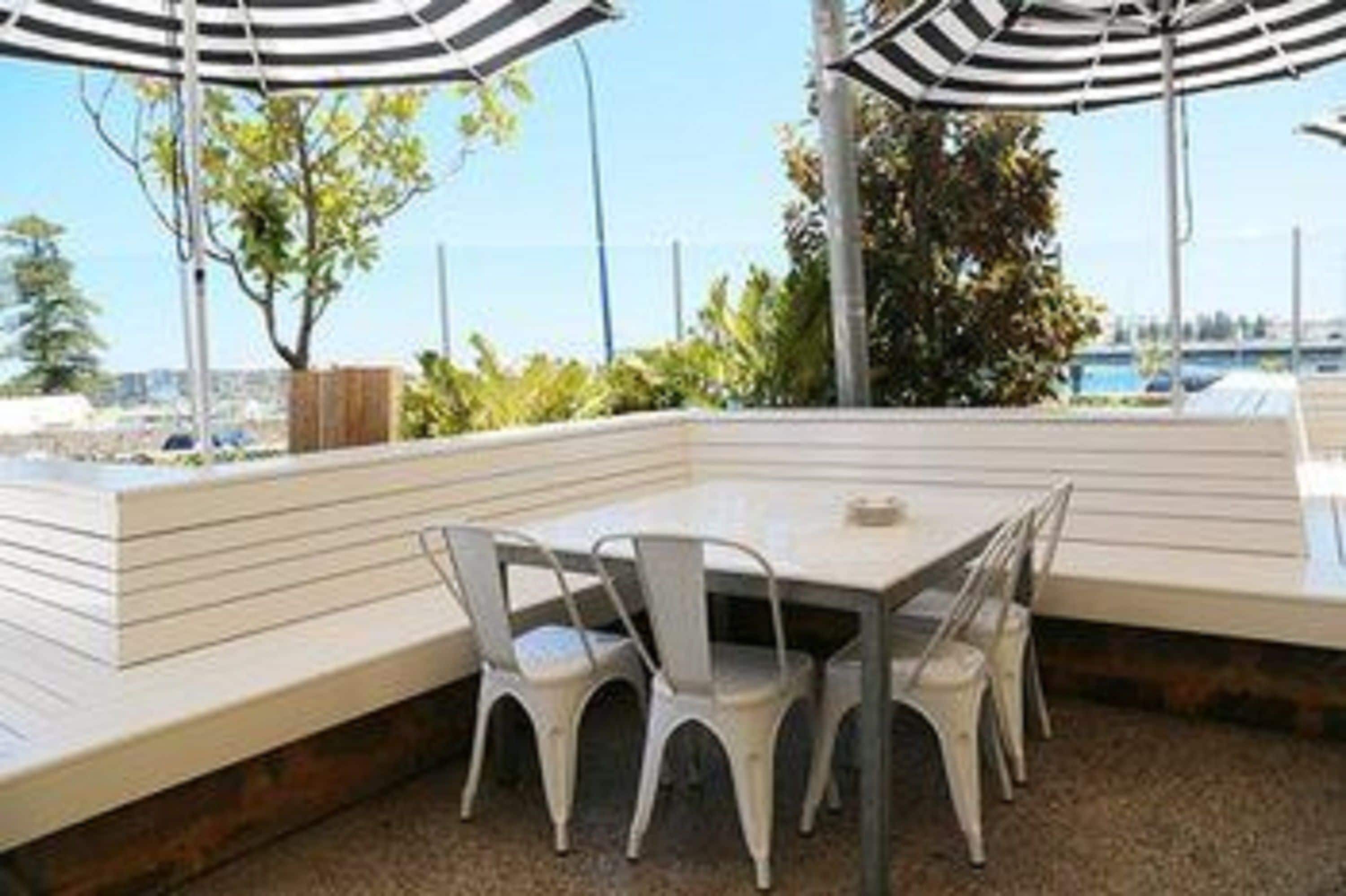 Un área de estar al aire libre con una mesa y sillas, rodeada por un muro bajo y un toldo a rayas.