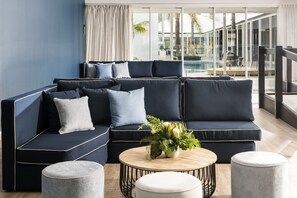 A modern living room with a dark blue sectional sofa, a round coffee table, and two ottomans. - Tradewinds Hotel Fremantle (East Fremantle)