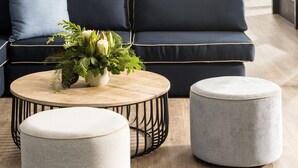 A modern living room with a dark blue sofa, two ottomans, a round coffee table, and a decorative plant centerpiece. - Tradewinds Hotel Fremantle (East Fremantle)