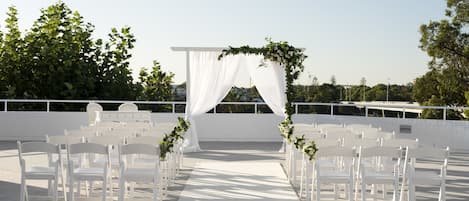 An outdoor wedding setup with white chairs and a white archway.