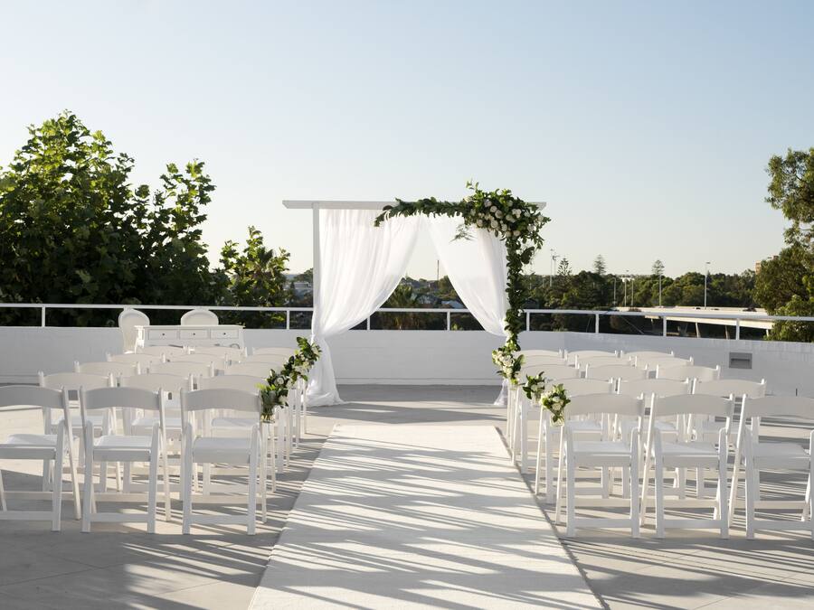 An outdoor wedding setup with white chairs and a white archway.
