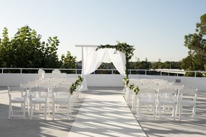 An outdoor wedding setup with white chairs and a white archway.