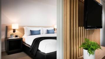 A modern hotel room with a bed, bedside tables, a flat-screen TV, and a potted plant.