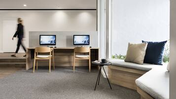 Un espace de bureau moderne comprenant deux bureaux, des chaises, une petite table avec une tasse et un canapé avec des coussins.