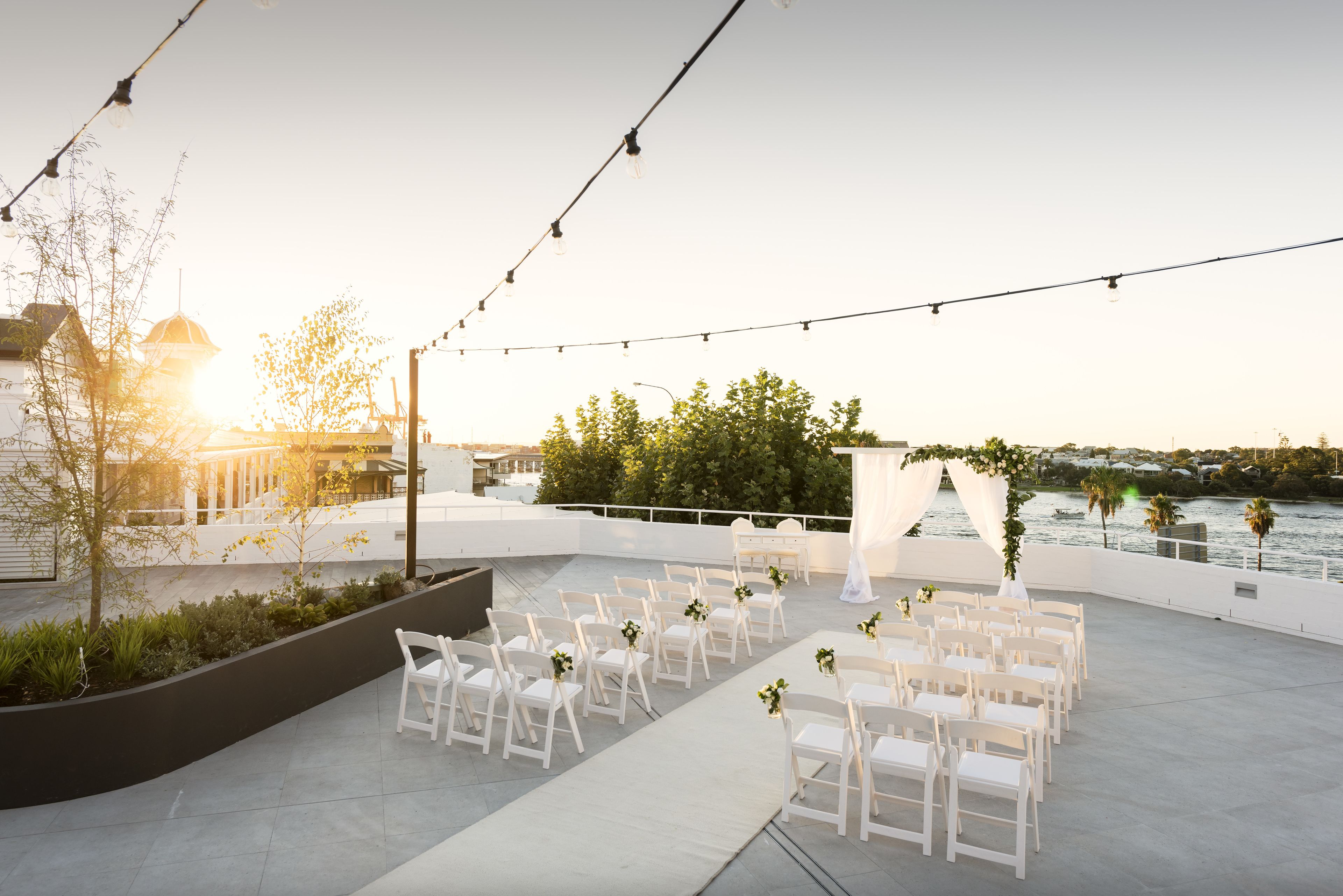 An outdoor wedding setup with white chairs and a white aisle, overlooking a body of water.