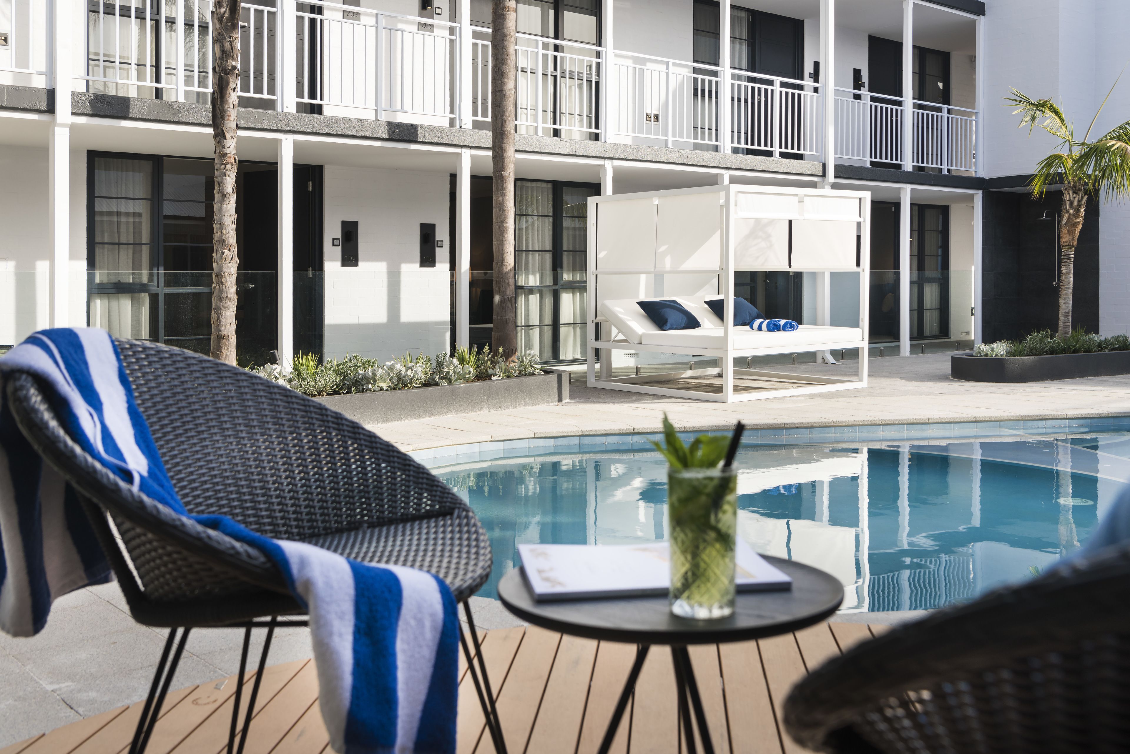 A poolside area with a lounge chair, a small table with a drink, and a white outdoor bed.