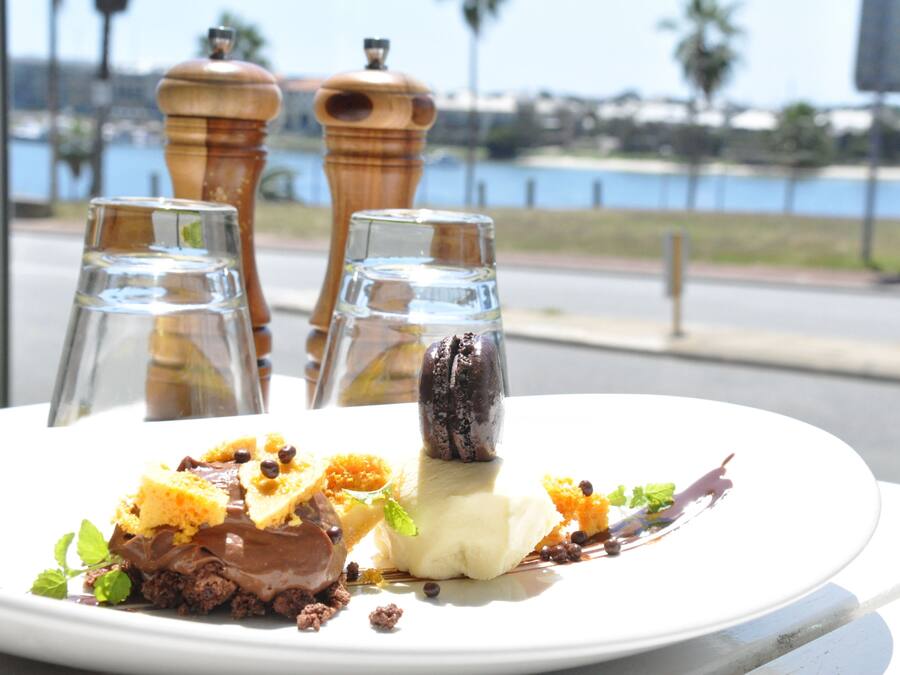 Un plato de postres con diferentes dulces y una vista del frente marítimo al fondo.