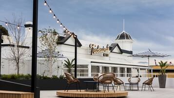 An outdoor seating area with wicker chairs and a table, a sign for 'The Whimsy Hotel', and a large umbrella.
