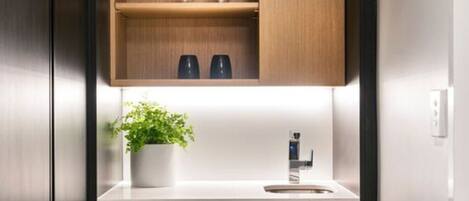 A compact kitchen with dark wood cabinets, a white countertop, a small potted plant, and a modern faucet.