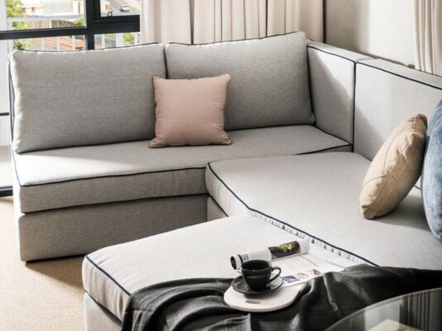 Ein modernes Wohnzimmer mit einem grauen Ecksofa, einem Glastisch und einer hängenden Pendelleuchte.