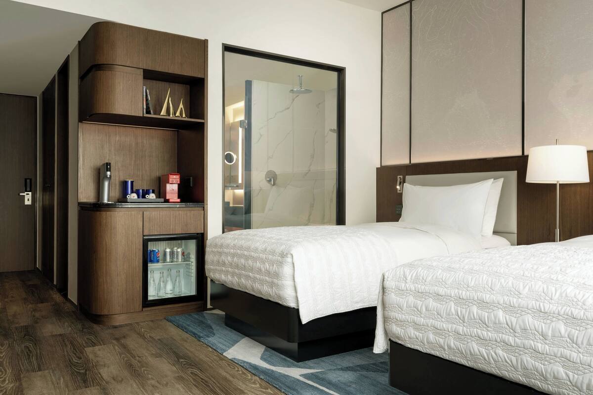 A hotel room with two beds, a minibar, a shower, and a wooden wardrobe.