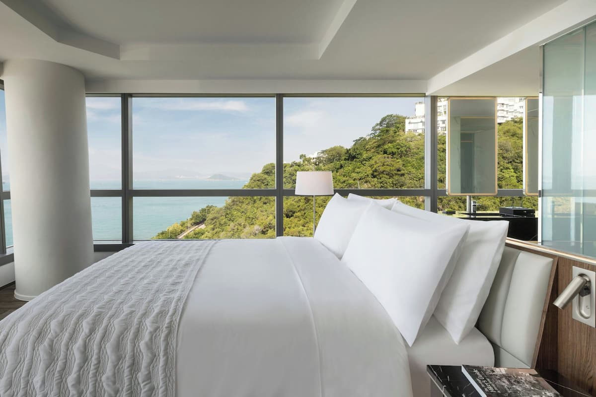 A modern hotel room with a large bed, a view of the sea, and a large window.