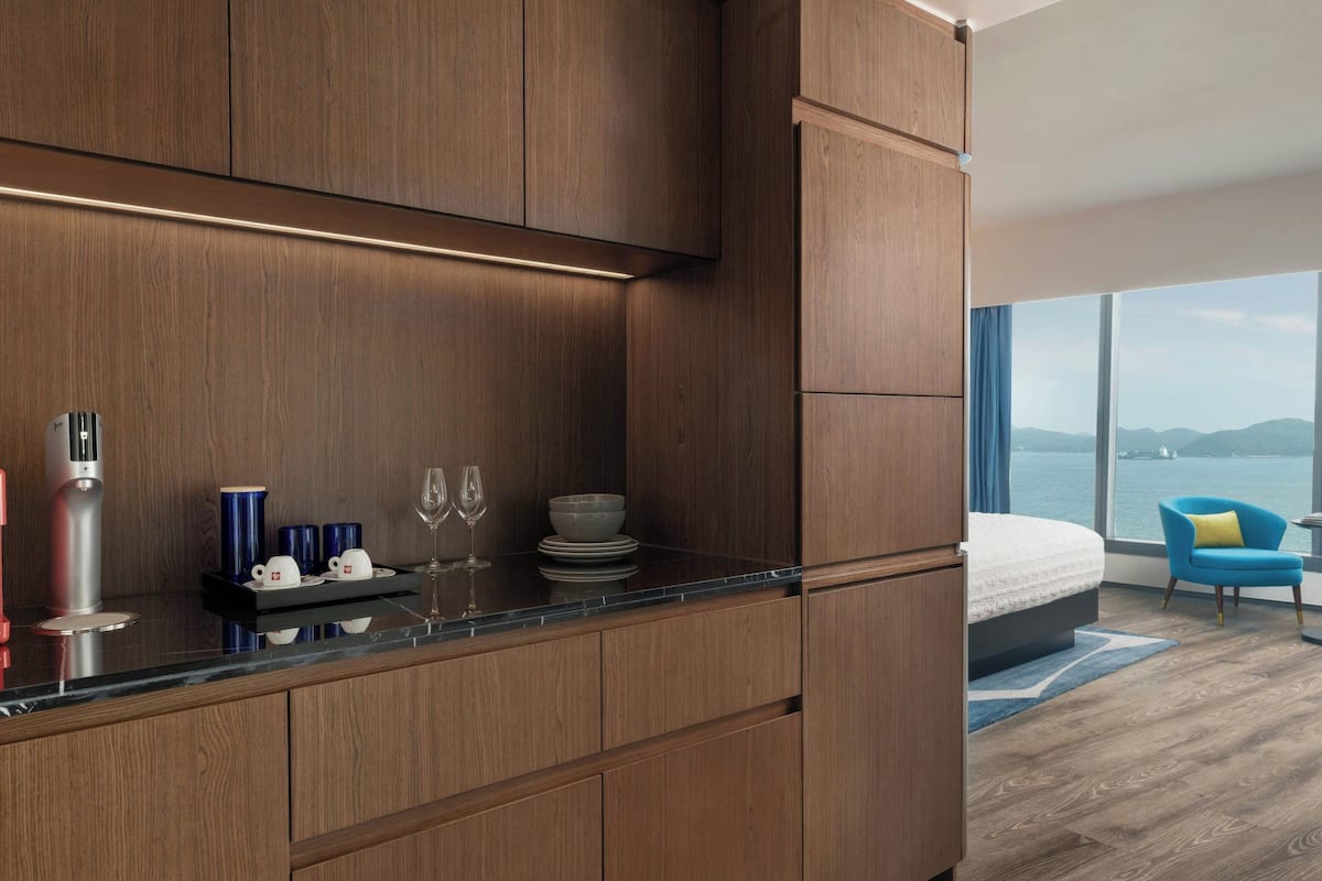 A modern kitchen with wooden cabinets, a countertop, and a view of the sea through large windows.