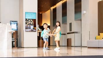 Welcome to our lobby, featuring a polished floor, digital reception desk, and cozy seating area with a sofa.
