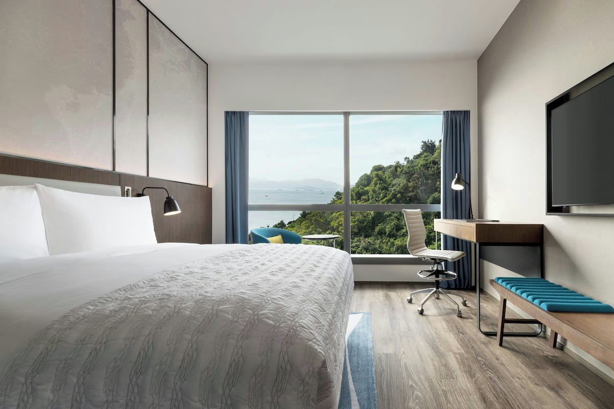A hotel room with a large bed, a desk, a chair, and a TV.