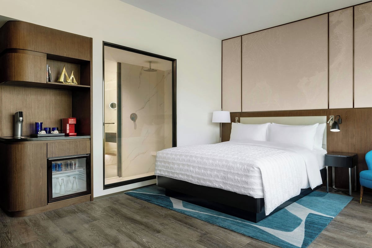 A hotel room with a bed, a minibar, a wardrobe, and a sliding door.