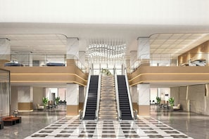 A spacious lobby with a central escalator, marble flooring, and a modern ceiling design.