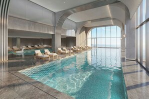 Una piscina interior moderna con agua cristalina, rodeada de sillones de descanso y vistas al cielo.