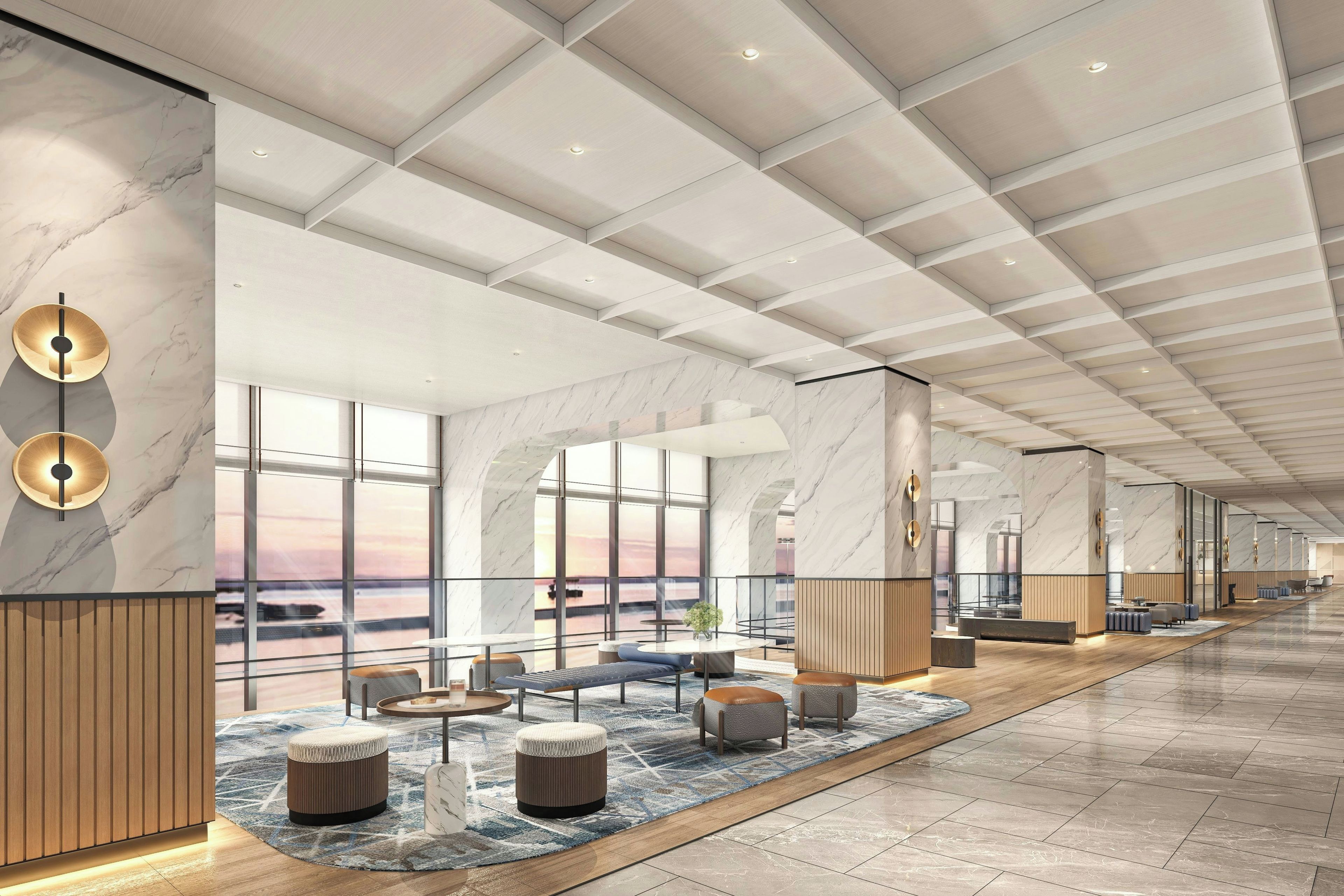 A spacious lobby with a high ceiling, marble walls, and large windows offering views of the sunset.