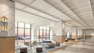 A spacious lobby with a high ceiling, marble walls, and large windows offering views of the sunset.