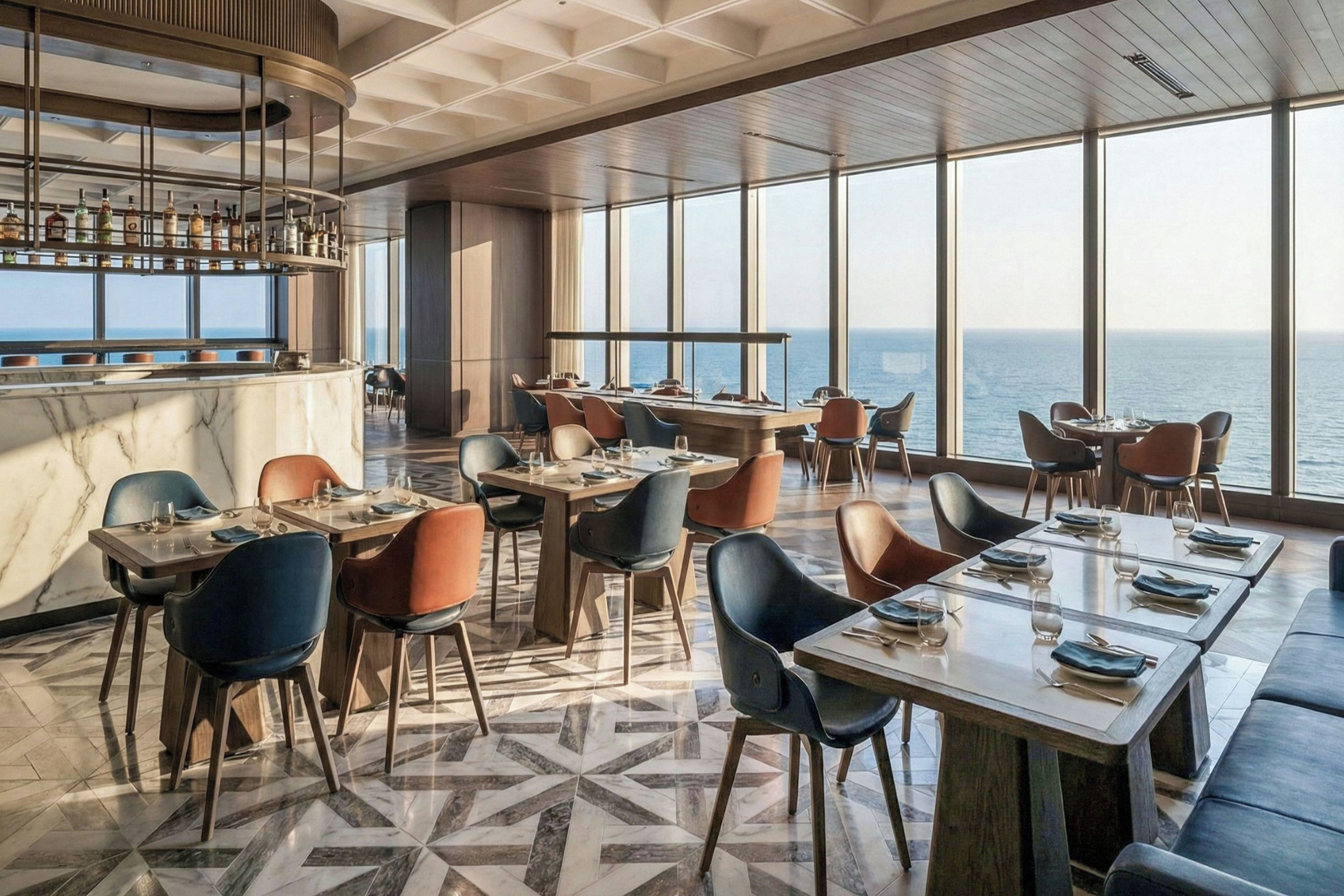 A restaurant with a view of the sea, featuring a bar area with bottles, and tables with chairs arranged for dining.