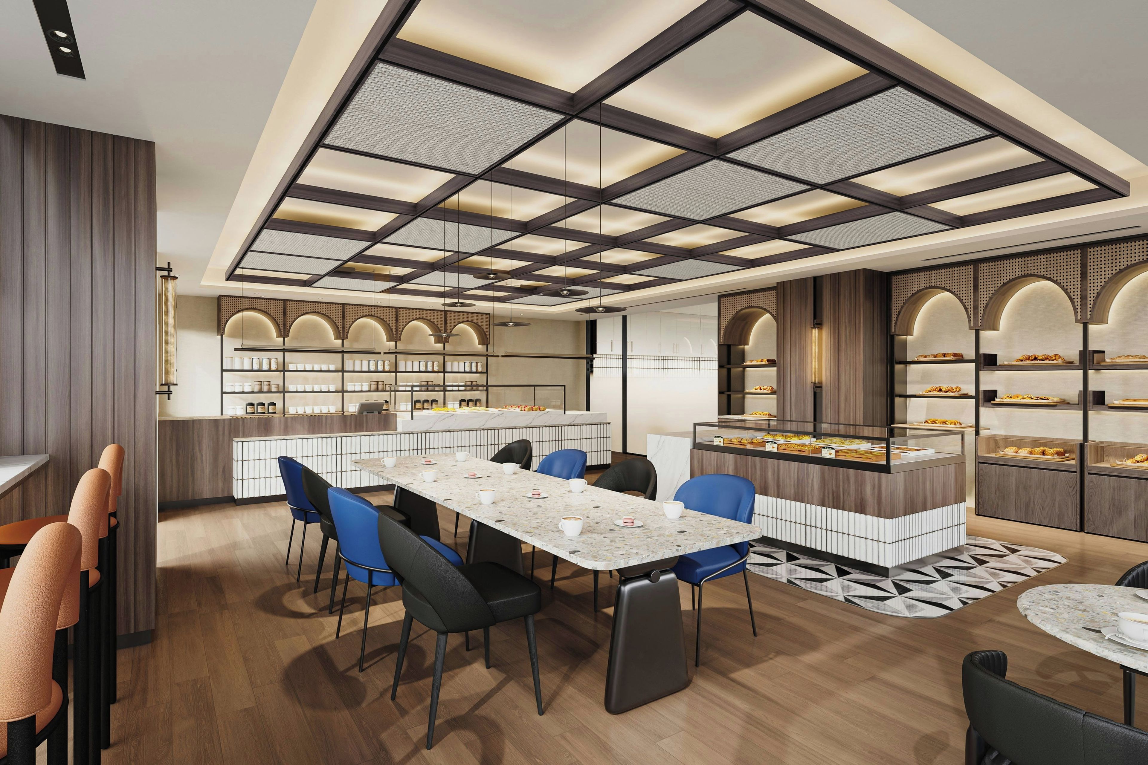A modern cafe with a long communal table, blue chairs, and a variety of baked goods displayed in the background.