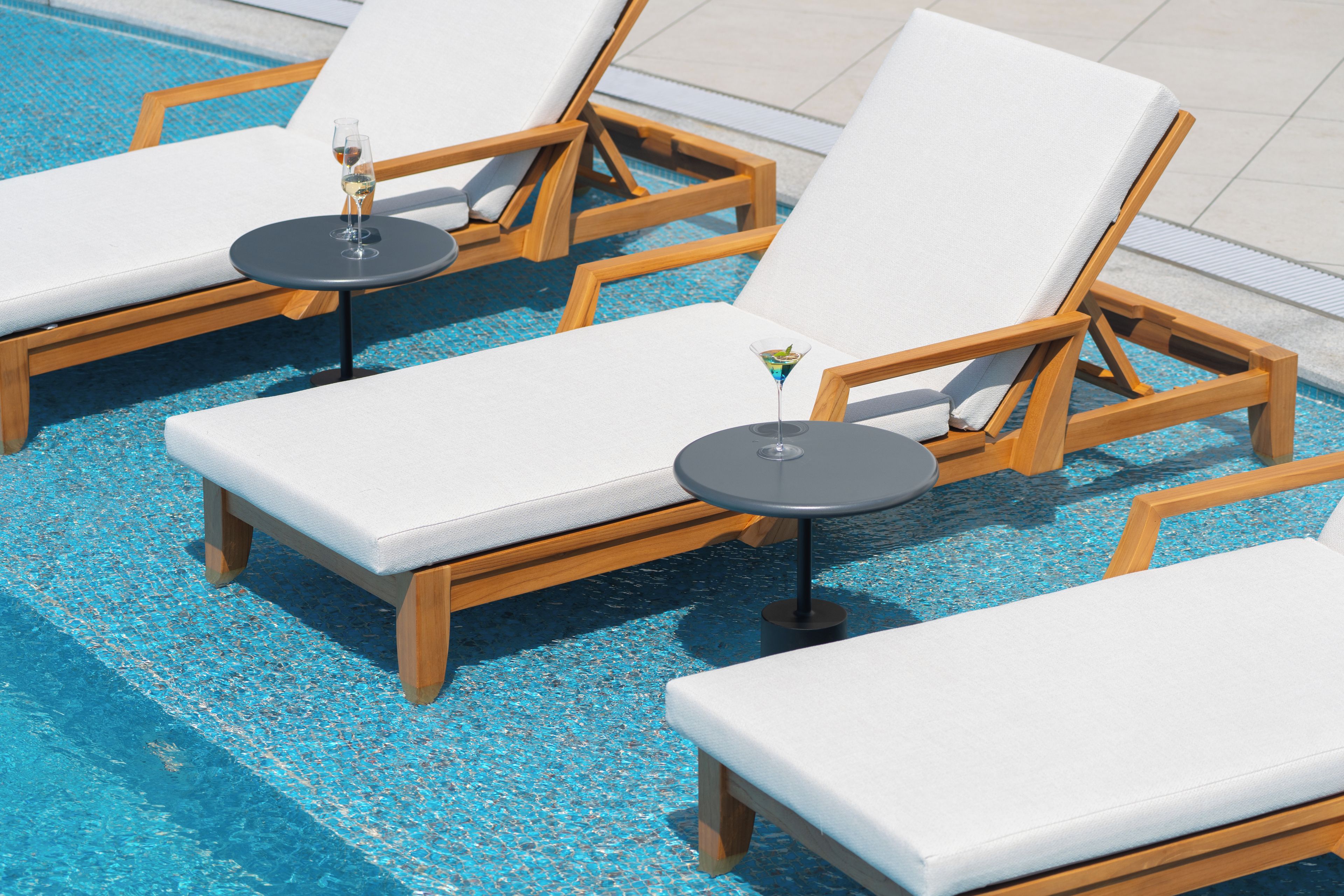 A poolside area with lounge chairs and tables, some with drinks.