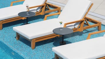 A poolside area with lounge chairs and tables, some with drinks.