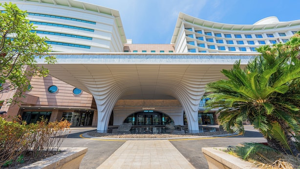 A modern hotel entrance with a curved overhang and a sign reading 'Sheraton.'