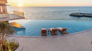 A pool area with lounge chairs and a view of the sea at sunset.