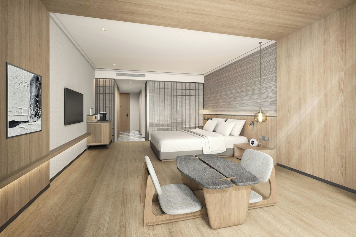 Un dormitorio moderno con cama, mesita de noche y una zona de estar con banco y sillón.