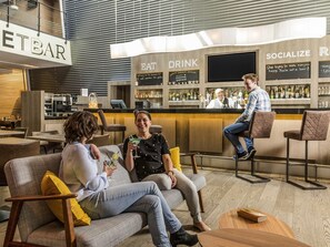 A modern bar area with seating, a bar counter, and a bartender. - Novotel Mechelen Centrum (Mechelen)