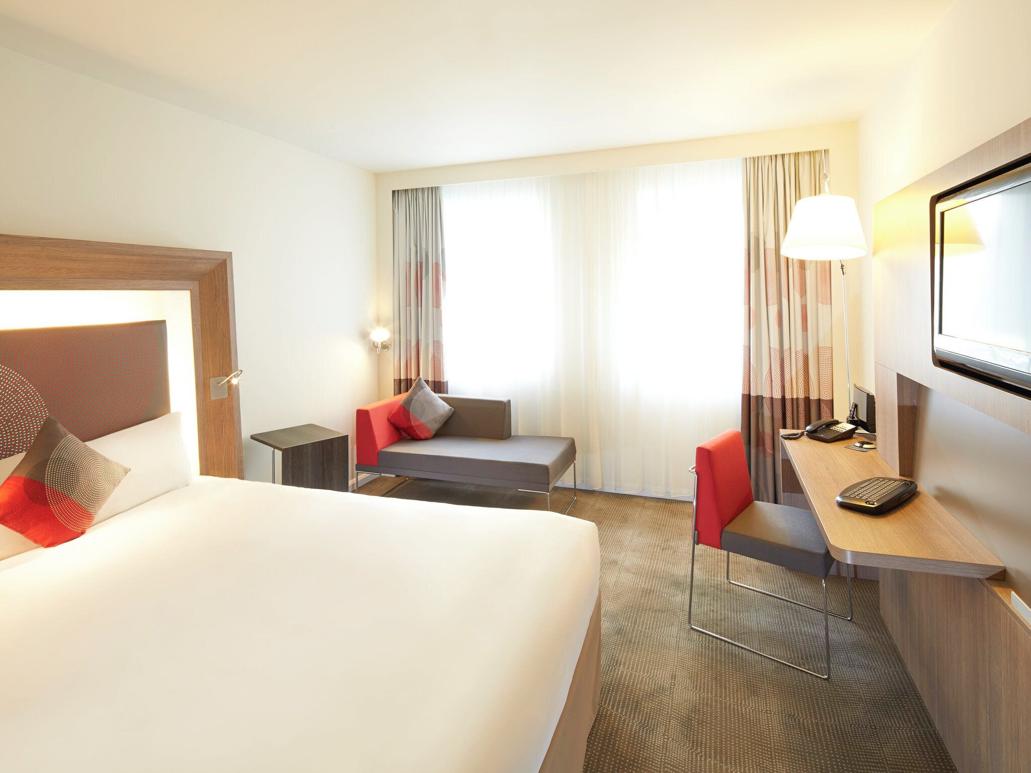 Habitación de hotel con cama, escritorio, silla, una mesita, lámpara y televisión.