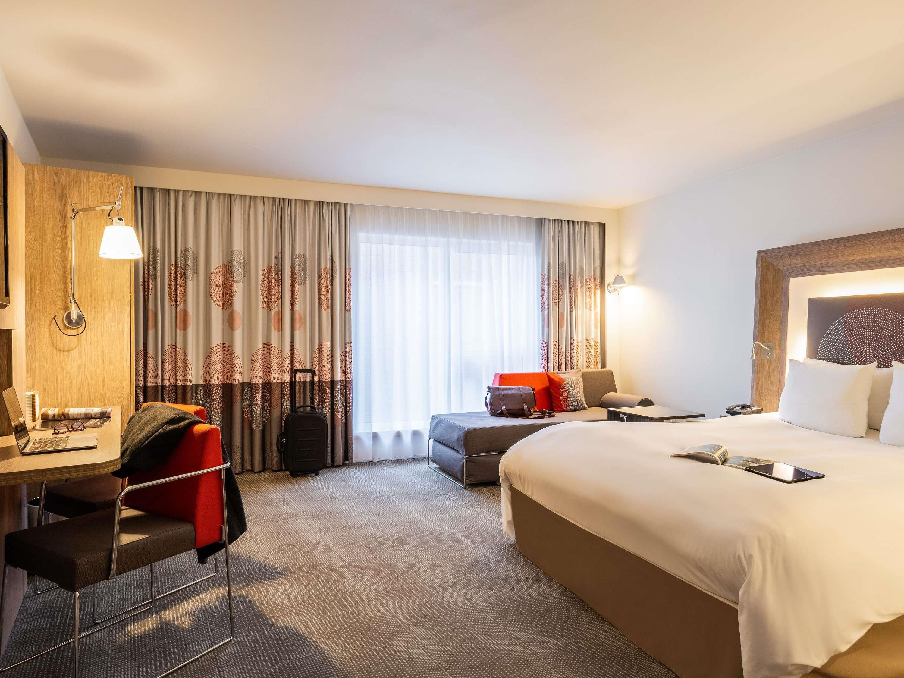 Een hotelkamer met een bed, een bureau, een stoel, een koffer en een raam met gordijnen.