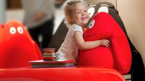 Un enfant est assis sur une chaise rouge, avec une pile de livres à côté de lui.