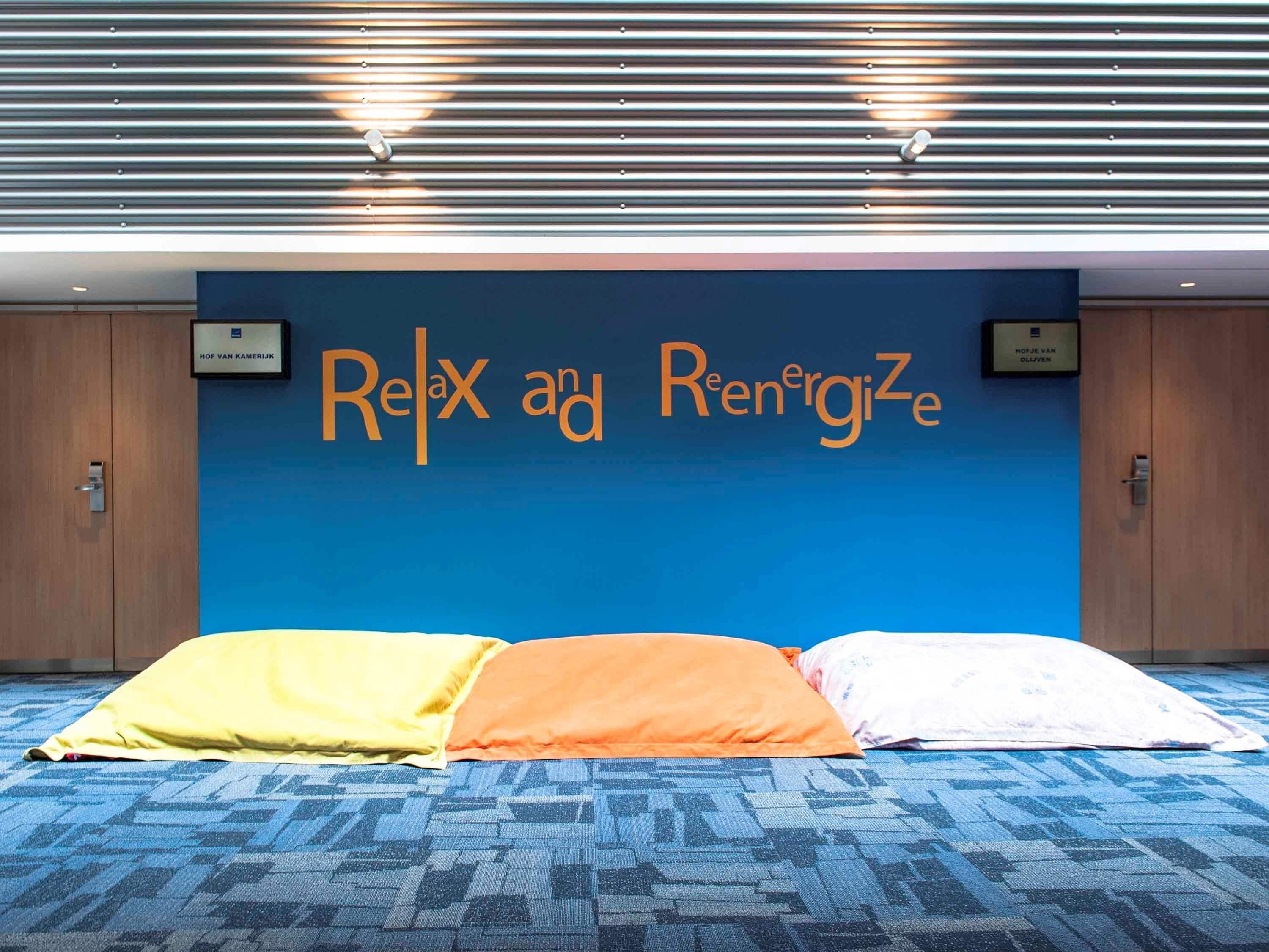 A room with a blue wall, a sign that reads "Relax and Recharge," and three pillows in yellow, orange, and white.