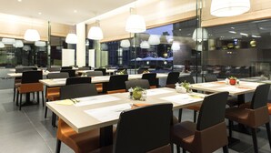 Un espace de restauration moderne, doté de plusieurs tables et chaises, de grandes fenêtres et d’un éclairage suspendu.