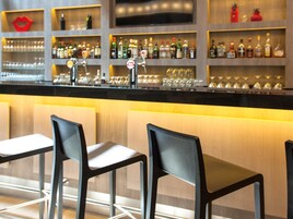 Una zona de bar con mostrador, estantes llenos de botellas, vasos y una decoración con pintalabios rojo.