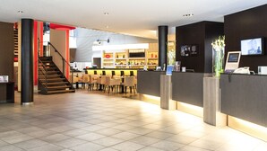Un hall d’hôtel moderne comprenant un comptoir d’accueil, un espace salon et un escalier menant à un autre étage.
